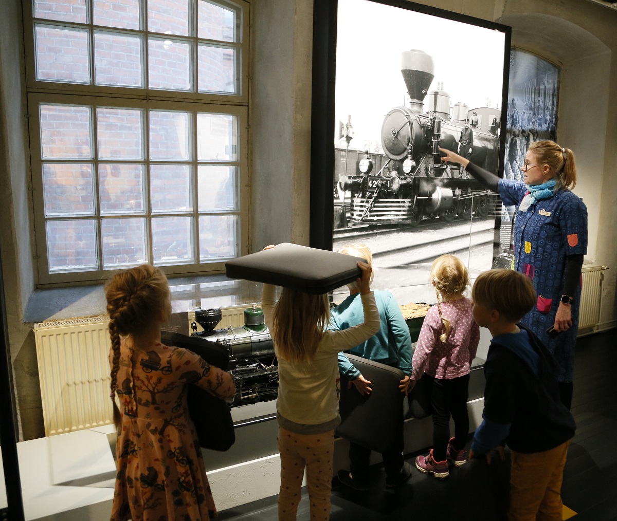 Museon opas näyttää lapsiryhmälle kuvaa höyryveturista.