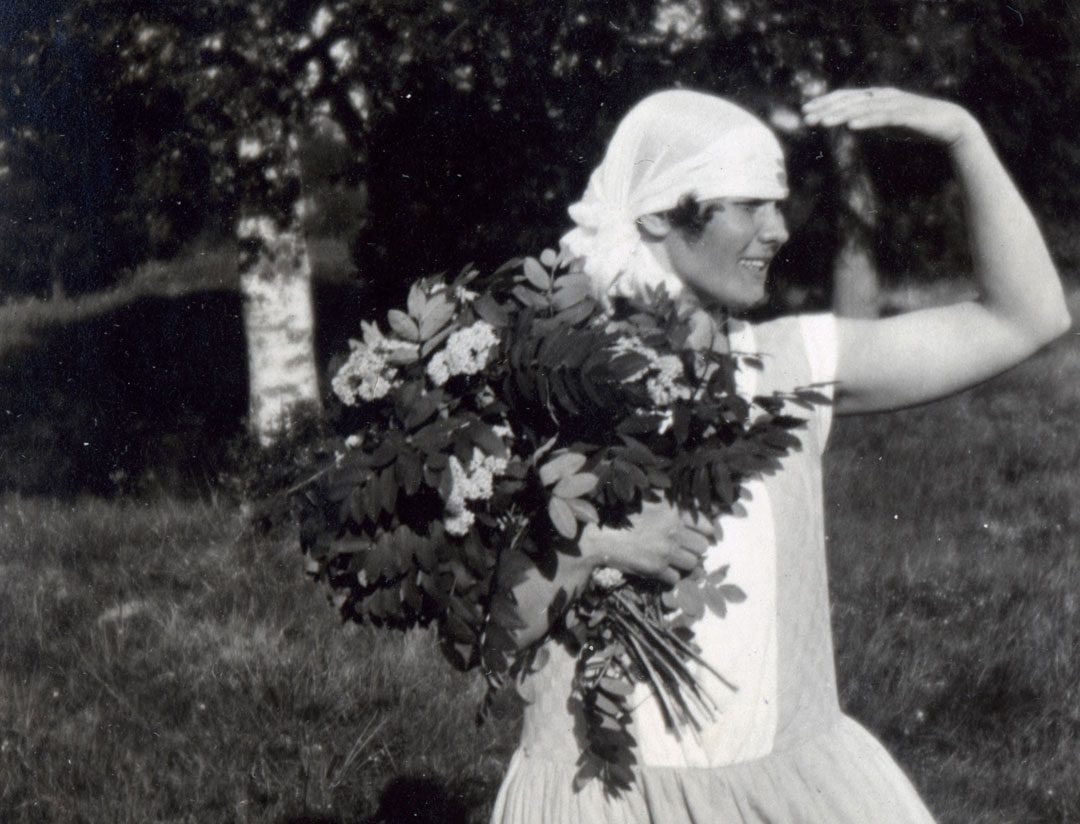 Nuori nainen kantaa suurta kukkakimppua ja suojaa kädellä silmiään auringolta