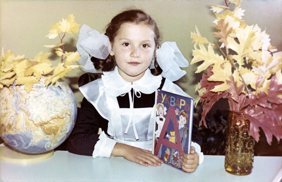 Pikkutyttö istuu pöydän ääressä käsissään venäjänkielinen aapinen