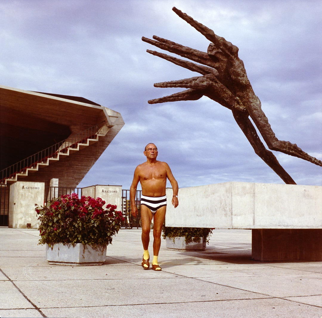 Nainen katsoo vasempaan toinen käsi nostettuna leualle. Hänen molemmilla puolillaan näkyy lapsen pää, kasvot haudattuina naisen olkapäiden taakse.