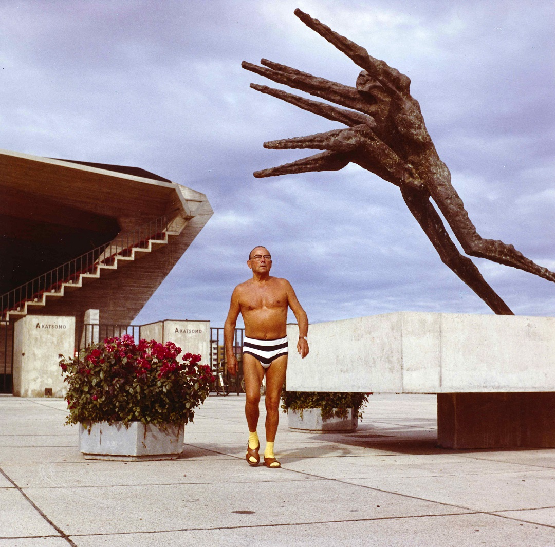 Nainen katsoo vasempaan toinen käsi nostettuna leualle. Hänen molemmilla puolillaan näkyy lapsen pää, kasvot haudattuina naisen olkapäiden taakse.